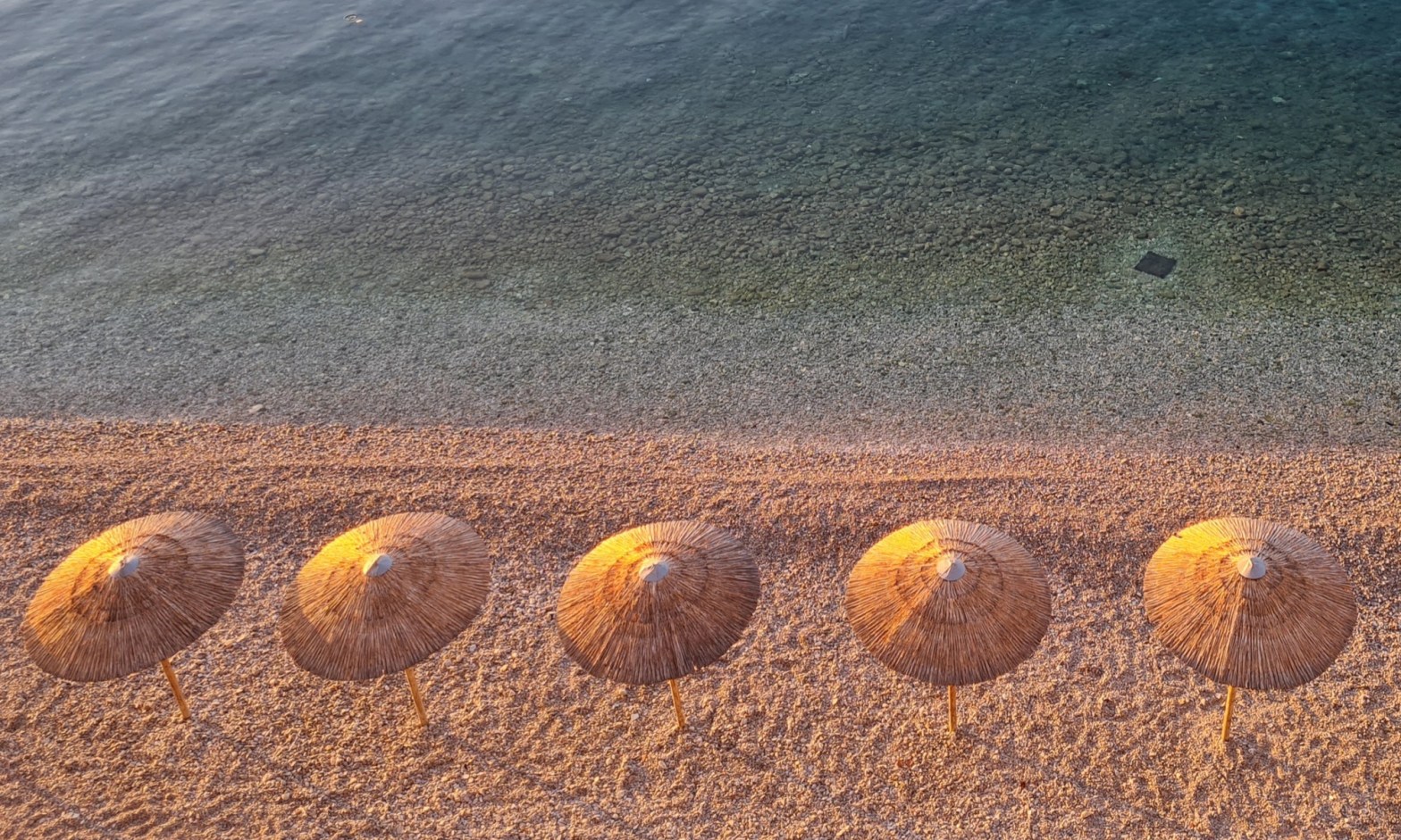 pictures in Greece during golden hour of traditional umbrellas and a clear sea with a pebble stone beach