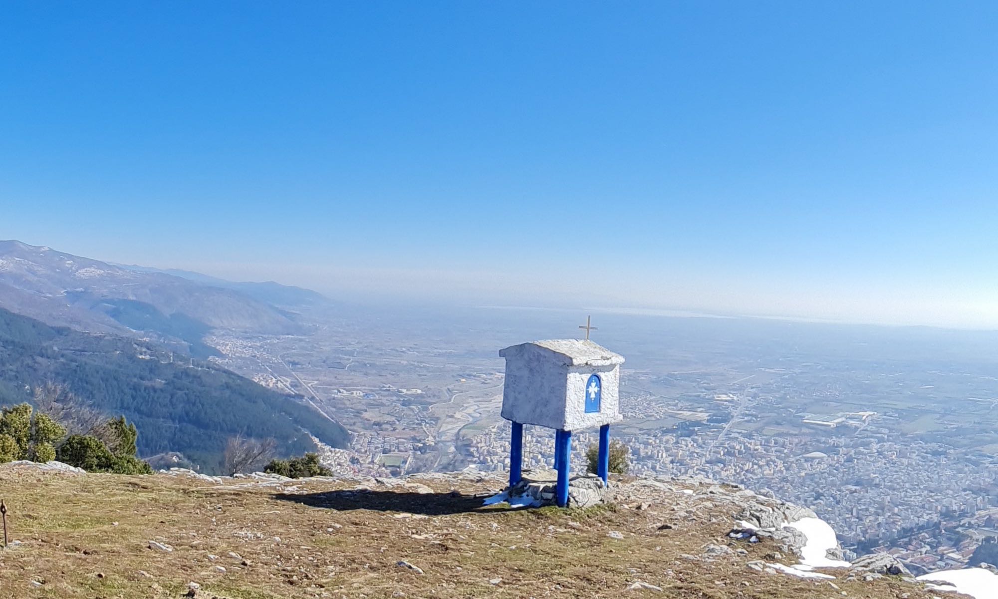 small church along the road in Greece on mountain cliff overlooking city blue sky